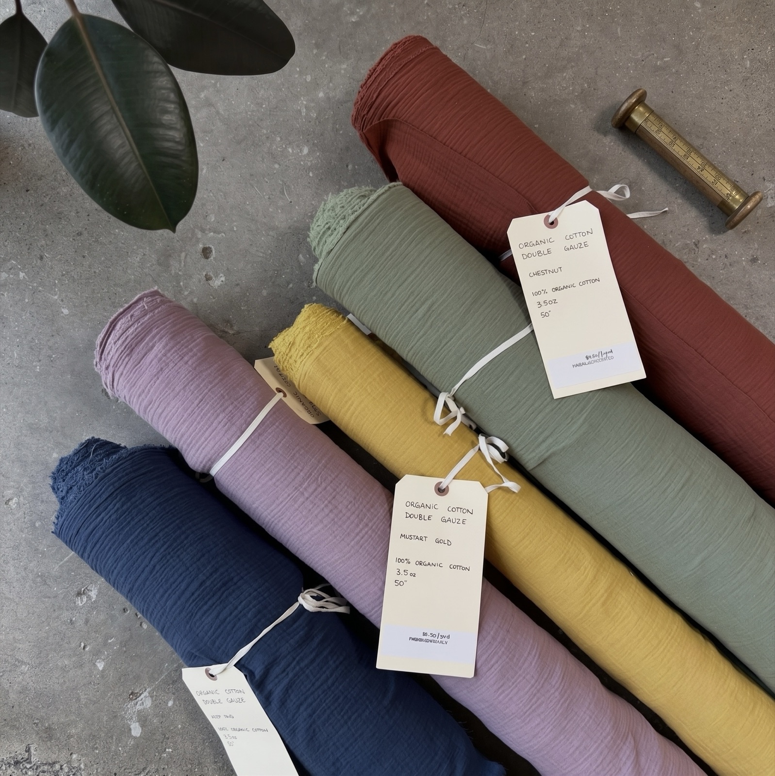 Rolls of organic cotton double gauze fabric in chestnut, sage, mustard, lilac, and navy