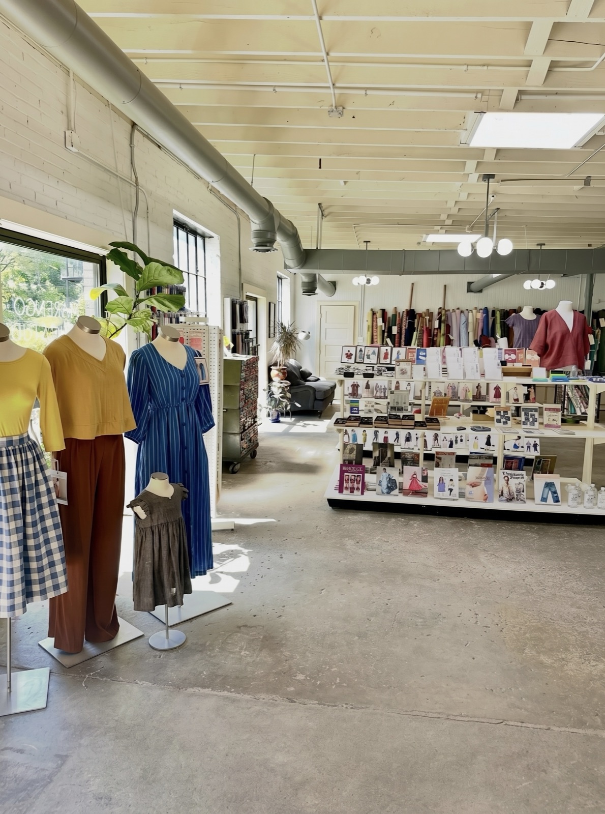 Shop interior with handmade garments on mannequins and shelves of sewing patterns